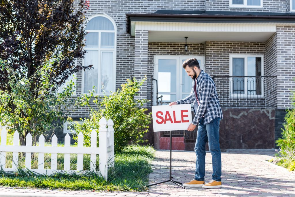 man putting sale sign in front of home